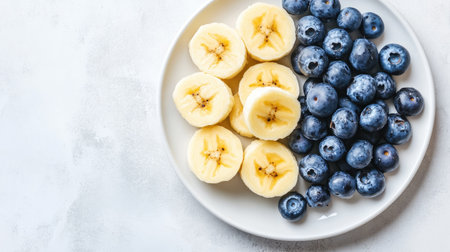A vibrant arrangement of sliced bananas and fresh blueberries on a white plate. This healthy snack option is rich in vitamins and antioxidants, perfect for a nutritious diet.の素材