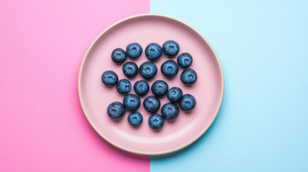 A vibrant arrangement of fresh blueberries on a pink plate creates a visually striking contrast against a blue background. Perfect for showcasing healthy eating.の素材