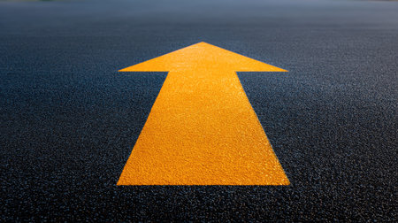 A close-up view of a bright yellow arrow painted on a freshly laid asphalt road. The vibrant color stands out against the dark surface, providing clear guidance for drivers and pedestrians. This image emphasizes safe navigation and urban transportation.の素材