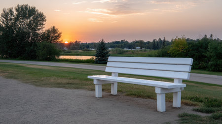 A serene white bench sits on the shore of a tranquil lake, surrounded by lush greenery, capturing the calming essence of a sunset in nature.の素材