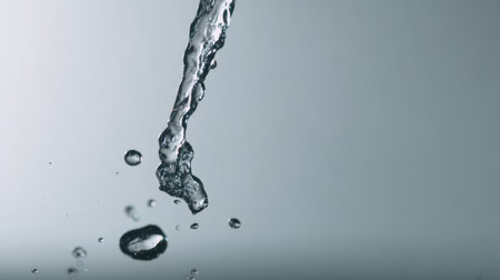 This image captures the elegant flow of crystal clear water droplets against a soft gray background, showcasing beauty, motion, and purity in a minimalist style.の素材