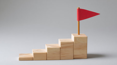 Stair steps made of wooden blocks leading to a flag icon, symbol of progress and achievement, isolated on blank backdropの素材