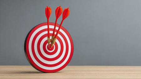 Target dartboard with arrows hitting the bullseye placed on a desk, symbolizing achievement and business goals, clean background with copy spaceの素材