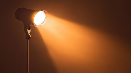 A dramatic orange spotlight effect, casting a golden hue in a dark room, creating intense contrasts of light and shadow. No text, no people.の素材