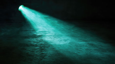 A green spotlight beam focused on a dark floor, creating a defined pool of light surrounded by shadow. No text, no people.の素材