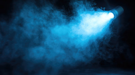Blue spotlight shining through fog, casting cool hues on a dark floor with smoke and lighting effects adding depth. No text, no people.の素材