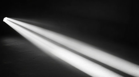 Bright spotlight illuminating a smooth surface, casting long, soft shadows in a dark room. The beam of light creates a focal point in an otherwise darkened space. No text, no people.の素材