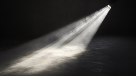 A single concert spotlight shining across the floor, casting a bright light surrounded by dark shadows in the empty venue. No text, no people.の素材