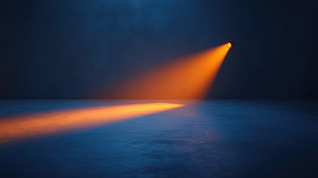 Spotlight in a dark room glowing in orange hues, with shadows forming across the floor as the light radiates outward. No text, no people.の素材