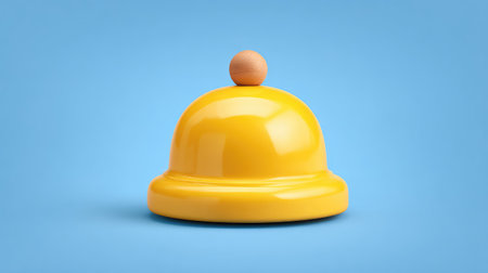 A bright yellow service bell with a wooden knob stands out against a soft blue background, perfect for concepts relating to hospitality, alertness, or customer service.の素材