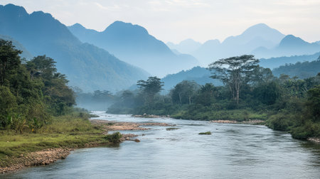 A peaceful river flowing through a serene valley, with misty mountains in the background. The vast landscape and open sky create ample space for copy.の素材