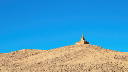 A peaceful stupa nestled in the middle of a desert landscape, the clear blue sky and dry earth surrounding it with empty spaceの素材