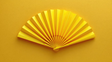 A vibrant yellow paper fan elegantly spread open against a matching yellow backdrop, ideal for summer themes, creative projects, or stylish presentations.の素材