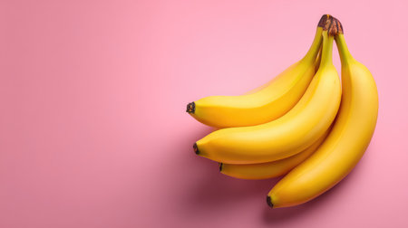Clean flat lay of yellow bananas on pastel pink background, positioned to allow central copy spaceの素材