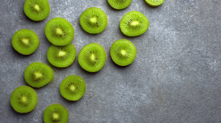 Bright green kiwi slices spread across textured gray stone surface, negative space availableの素材
