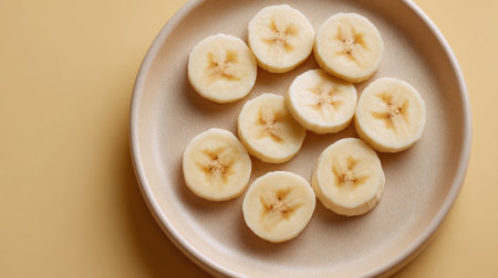 Fresh banana slices arranged randomly on a light-colored plate, top view with open backgroundの素材