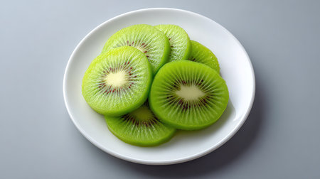 Fresh sliced kiwi arranged diagonally on a white plate, top view with copy space on one sideの素材