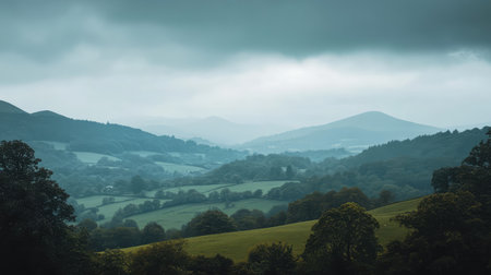 Scenic landscape showcasing lush green hills and misty mountains under a dramatic cloudy sky, illustrating the beauty of nature in a tranquil outdoor setting.の素材