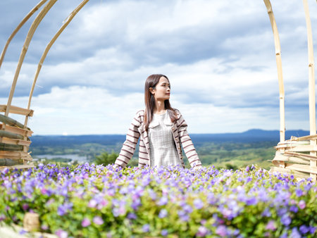 Woman stands amidst vibrant purple flowers, framed by natural archway. scenic landscape features rolling hills under cloudy sky, creating serene and picturesque atmosphereの写真素材