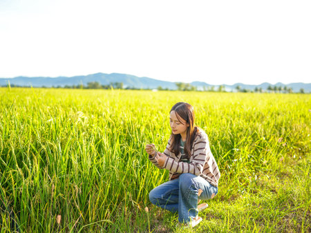 Young woman examines rice plants in lush green field under bright sunlight. serene landscape...