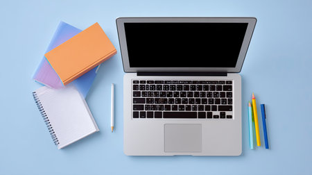 A flat lay view of a modern workspace featuring a laptop, colorful notebooks, and stationery items on a soft blue background, perfect for productivity and study.の素材