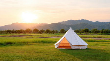 A peaceful glamping tent sits on lush green grass against a stunning mountain backdrop as the sun sets, offering a perfect escape into nature's beauty.の素材