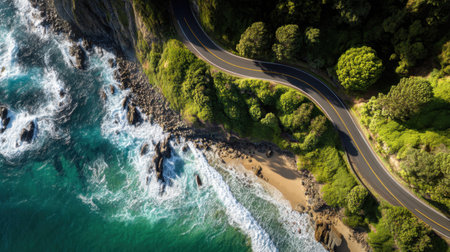 Captivating aerial perspective showcasing a winding road next to a vibrant turquoise ocean, sandy beach, and rich greenery, highlighting the beauty of nature.の素材
