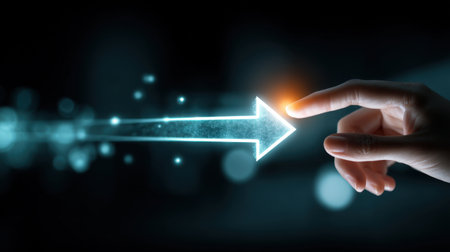 A close-up view of a hand reaching out to touch a glowing digital arrow, representing innovation and progress in technology against a dark background.の素材