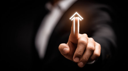 A businessman points at a glowing upward arrow, representing growth and success. The dark background enhances the impact of the gesture, highlighting ambition.の素材