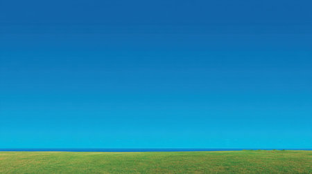 A stunning panorama showcasing a rich green field under a vivid blue sky meeting a tranquil water body at the horizon, perfect for nature-themed projects.の素材