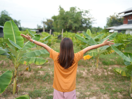 A young woman stands in a lush green banana plantation with her arms open wide, embracing nature's beauty. This serene moment captures the essence of freedom and joy in rural life.の写真素材