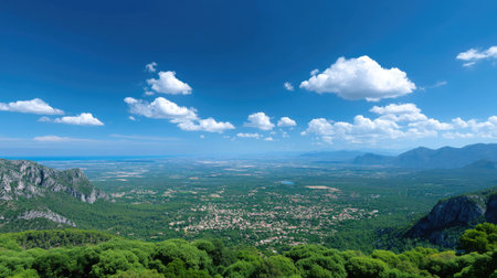 A breathtaking view captures a serene mountain landscape surrounded by lush greenery and a brilliant blue sky dotted with fluffy clouds.の素材
