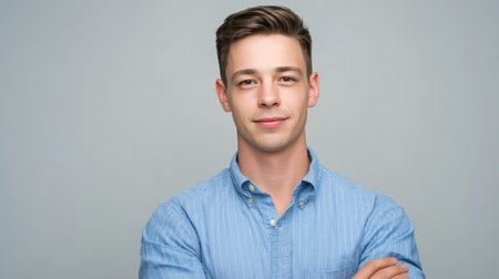 A portrait of a young man exuding confidence with crossed arms, dressed in a blue striped shirt, set against a light backdrop, ideal for showcasing modern professionalism and approachability.の素材