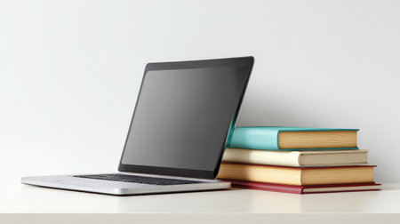 A sleek modern laptop sits next to a vibrant stack of books on a minimalist desk. This image captures the essence of study and productivity in a clean, organized environment.の素材