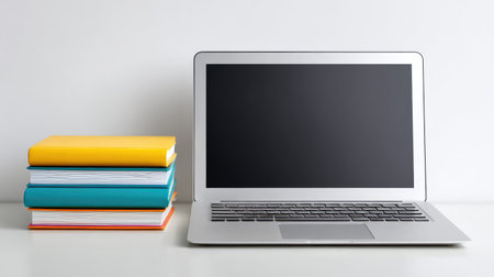 A sleek laptop positioned next to a vibrant stack of books on a minimalist desk, ideal for study sessions or enhancing productivity in a modern workspace environment.の素材