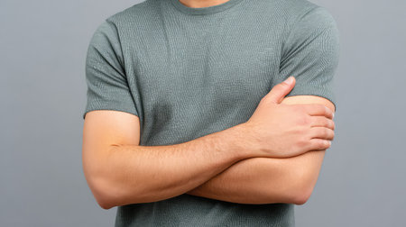 Portrait of a confident young man with arms crossed, dressed in a gray t-shirt, set against a neutral gray background, showcasing a blend of self-assuredness and casual style.の素材