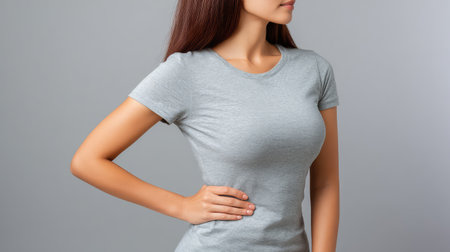 A young woman showcases a fitted gray t-shirt in a stylish pose, highlighting fashion and confidence against a simple, neutral background.の素材