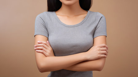 A confident young woman with arms crossed poses in a trendy grey top against a soft brown background, radiating strength and self-assurance ideal for lifestyle and fashion projects.の素材
