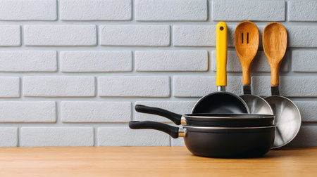 A collection of kitchen utensils featuring frying pans, wooden spoons, and ladles displayed against a stylish gray wall, perfect for modern cooking enthusiasts.の素材