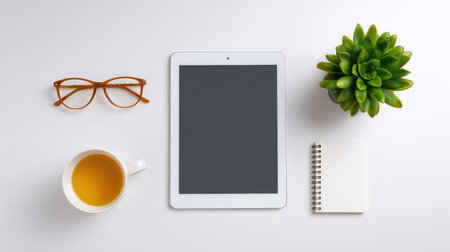 This stylish workspace flat lay showcases a tablet, glasses, succulent plant, notebook, and tea cup on a clean white surface, perfect for productivity and relaxation.の素材