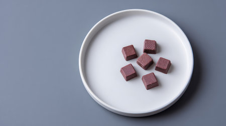 This image features a collection of square chocolate cubes arranged on a sleek white plate, set against a minimalist gray background, ideal for food-related content.の素材