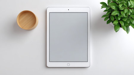 A sleek tablet rests on a white desk, accompanied by a wooden bowl and a green plant, creating a serene and organized workspace ideal for productivity and creativity.の素材