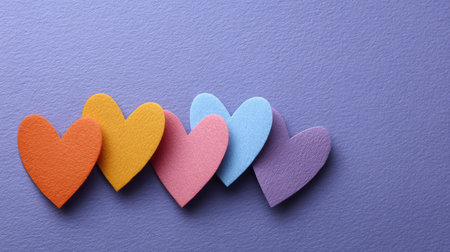 A collection of colorful paper hearts on a purple background, ideal for representing love and friendship in creative projects, digital art, or festive celebrations.の素材