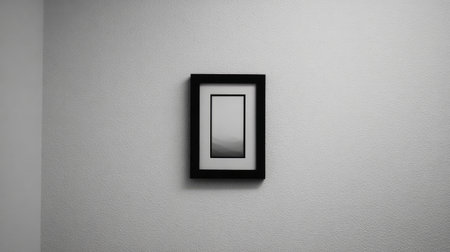 A minimalist black frame hung low on a smooth wall with surrounding negative spaceの素材