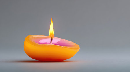 A vibrant yellow and pink candle featuring a flickering flame, set against a smooth gray background, creates a warm and inviting atmosphere for relaxation and meditation.の素材