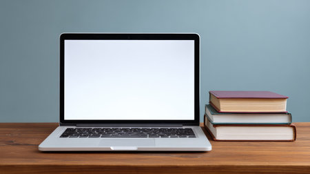 A sleek laptop sits atop a wooden desk beside a stack of colorful books, creating a stylish workspace. Ideal for concepts related to education and remote work.の素材