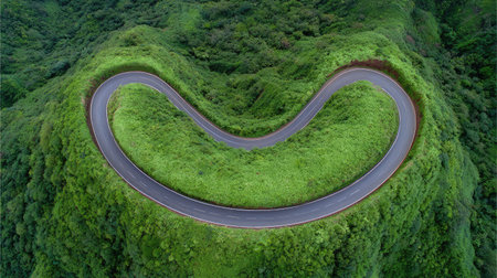 A stunning aerial view of a curving road surrounded by vibrant green hills, showcasing the beauty of nature and inviting viewers to explore this picturesque landscape.の素材