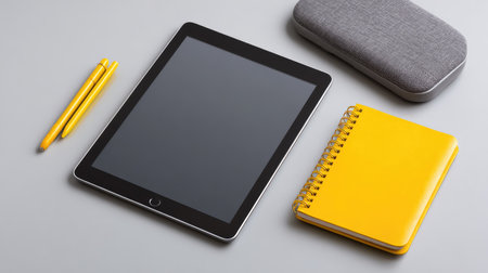 A modern workspace setup showcases a blank tablet, bright yellow notepad, and essential stationery, perfect for enhancing creativity and productivity in any environment.の素材