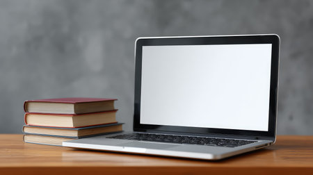 A modern laptop is showcased on a wooden table, accompanied by stacks of books, set against a gray background, capturing the essence of a productive workspace.の素材
