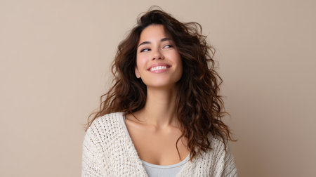 Portrait of a cheerful young woman with curls wearing a cozy sweater. She radiates happiness and confidence against a soft, neutral background.の素材